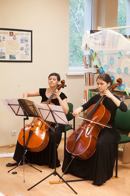 Na zdjęciu dwie siedzące kobiety, grające na wiolonczelach.
