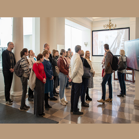 Uczestnicy stoją w holu Biblioteki i słuchają przewodnika.