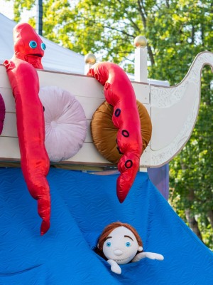 Zdjęcia maskotki ze spektaklu. Imitacja dziecka w wodzie, a obok na białej łodzi kraken.