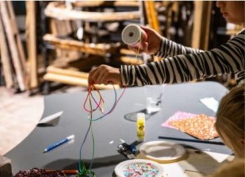 ręce dziecka trzymającego szpule z wstązką na stołem z innymi materiałami plastycznymi