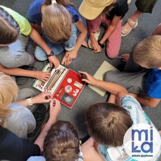 zdjecie z góry na którym widać dzieci siedzące na podłodze, wyciągają przybory z otwartego pudełka