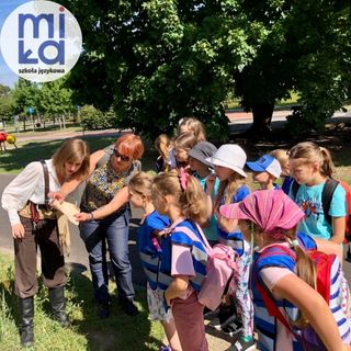 dzieci przypatrujące sie przedmiotowi trzymanemu przyz opiekuna w plenerze