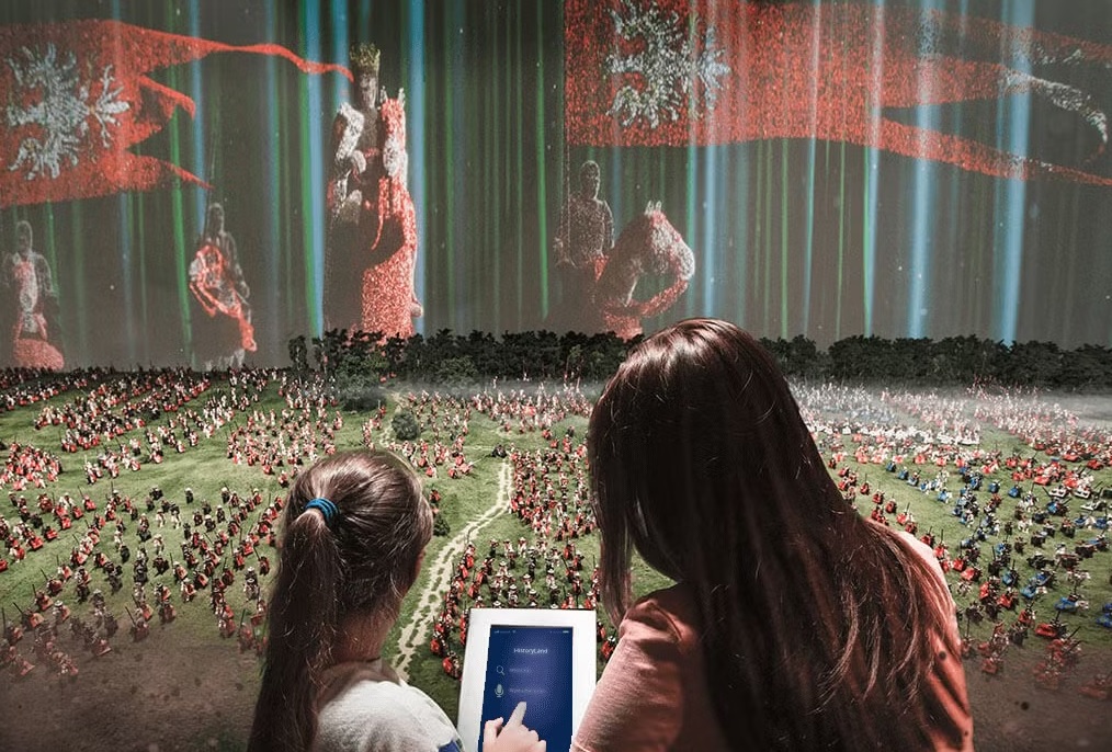 dwie osoby z interaktywnym tabletem przy makiecie Bitwy pod Grunwaldem