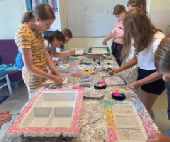 Zdjęcie przedstawia grupę dzieci, która zebrana wokół stołu wykonuje rękodzieło.