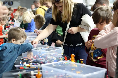 Dzieci siedzą przy stołach i układają klocki Lego.