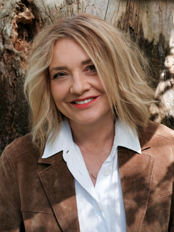 na zdjęciu uśmiechnięta kobieta z włosami do ramion, w białej bluzce i jasnej kurtce