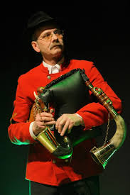 Na zdjęciu dudziarz w czerwonym ubraniu trzymający instrument muzyczny.