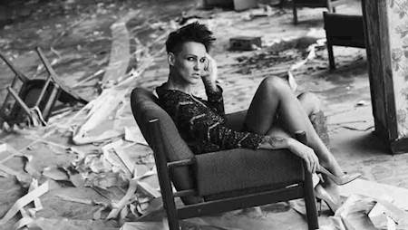 Artystyka siedzi w szpilkach i skuience na krześle, dookoła bałagan "remontowy". Zdjęcie czarno-białe.