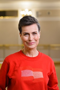 Zdjęcie uśmiechniętej Danuty Stenki w czerwonym swetrze. Jasne tło.