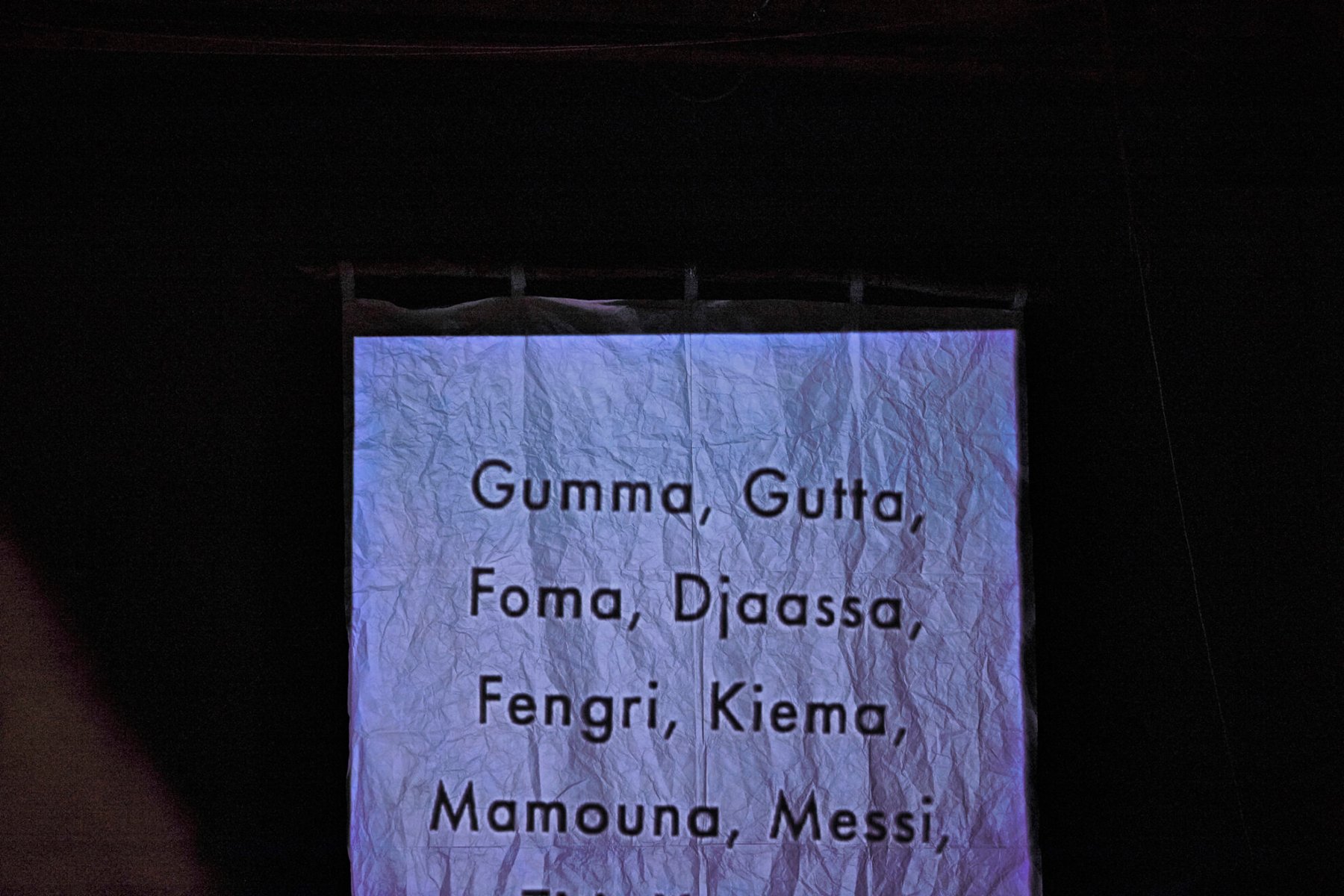 .Pognieciona kartka paperu, na której napisanych jest kilka słów, np. Gumma, Gutta, Foma. Czarne tło.