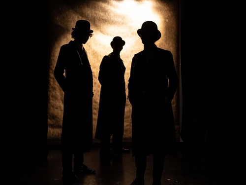 Zarys trzech postaci, za nimi jasna poświata.