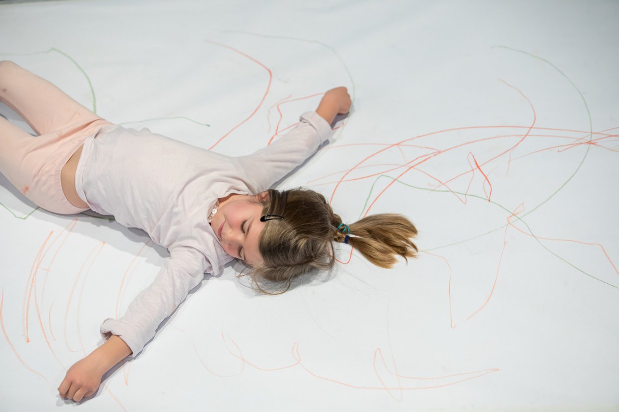 Zdjęcie dziewczynki leżącej z rozłożonymi rękami na dużym arkuszu papieru popisanego kredkami.