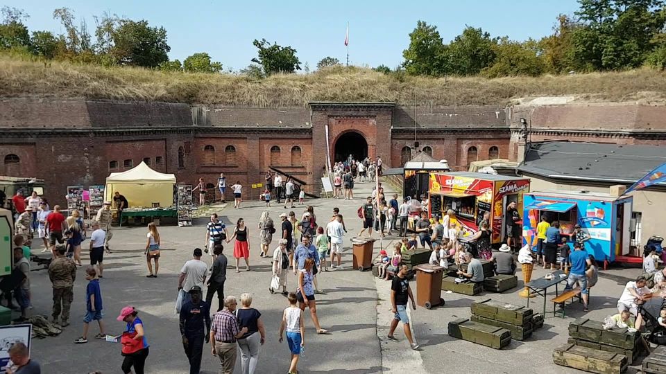 Ludzie chodzący po terenir fortu pomiędzy budkami z jedzeniem, straganami i innymi atrakacjami.