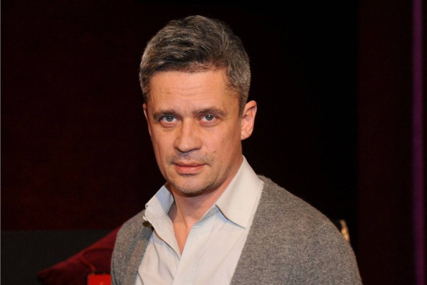 Zdjęcie uśmiechniętego mężczyzny w średnim wieku, ubranego w jasną koszulę i szary sweter