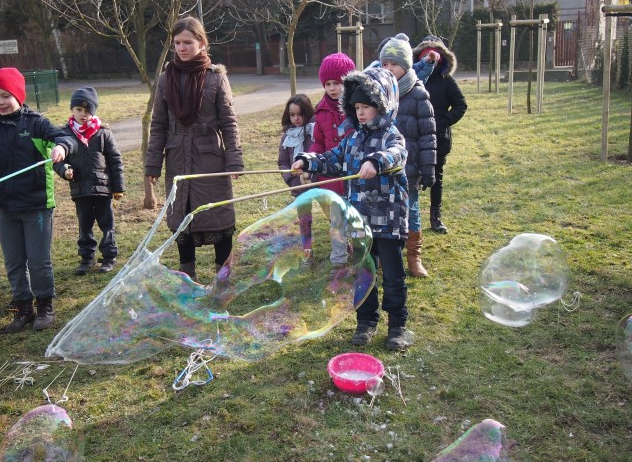 Zdjęcie przedstawia bawiące się dzieci na dworze z bańkami mydlanymi na półkolonii.