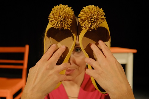 Kobieta trzyma w rękach dwa damskie buty z pomponami, zakrywa nimi część twarzy.