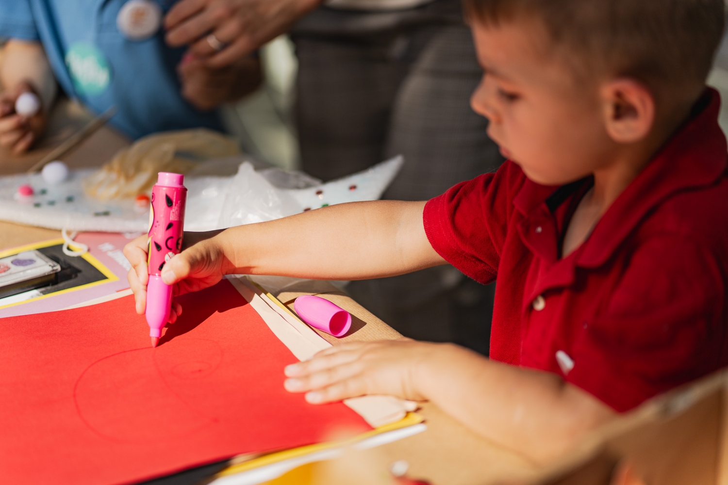 Zdjęice chłopca rysującego flamastrem na czerwonej kartce papieru.