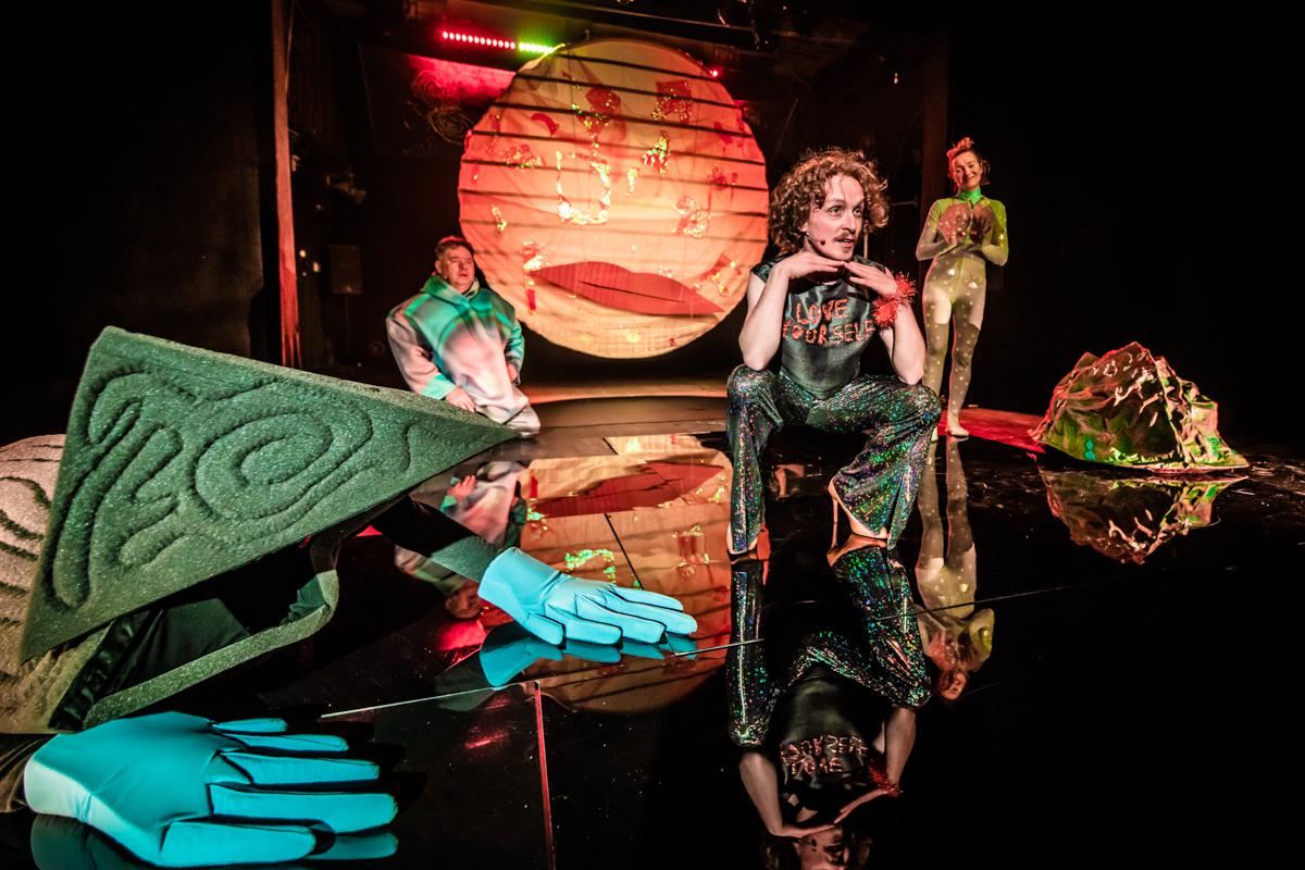 Zdjęcie trzech aktorów na scenie wśród elementów scenicznych dekoracji.