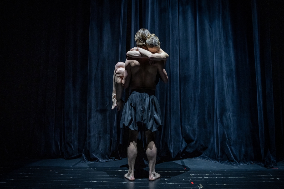 na scenie stoi tancerz, odwrócony tyłem, na rękach trzyma kobietę, która pochyla głowę do jego ramienia i obejmuje go za szyję