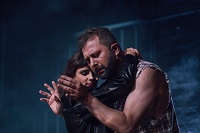 Kobieta i mężczyzna w uścisku, mężczyzna patrzy na swoje dłonie. Ciemno-niebieskie tło.