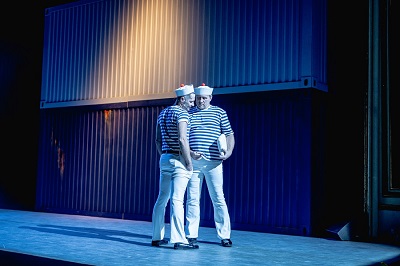 Na scenie dwóch mężczyzn stojących blisko siebie, w strojach przypominających marynarskie. Zdjęcie w niebiesko-błękitnych kolorach.