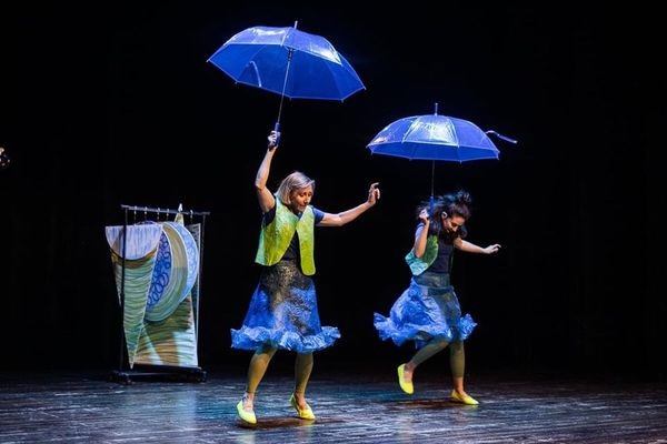 Dwie kobiety na scenie, każda z nich trzyma nad głową granatowy parasol.