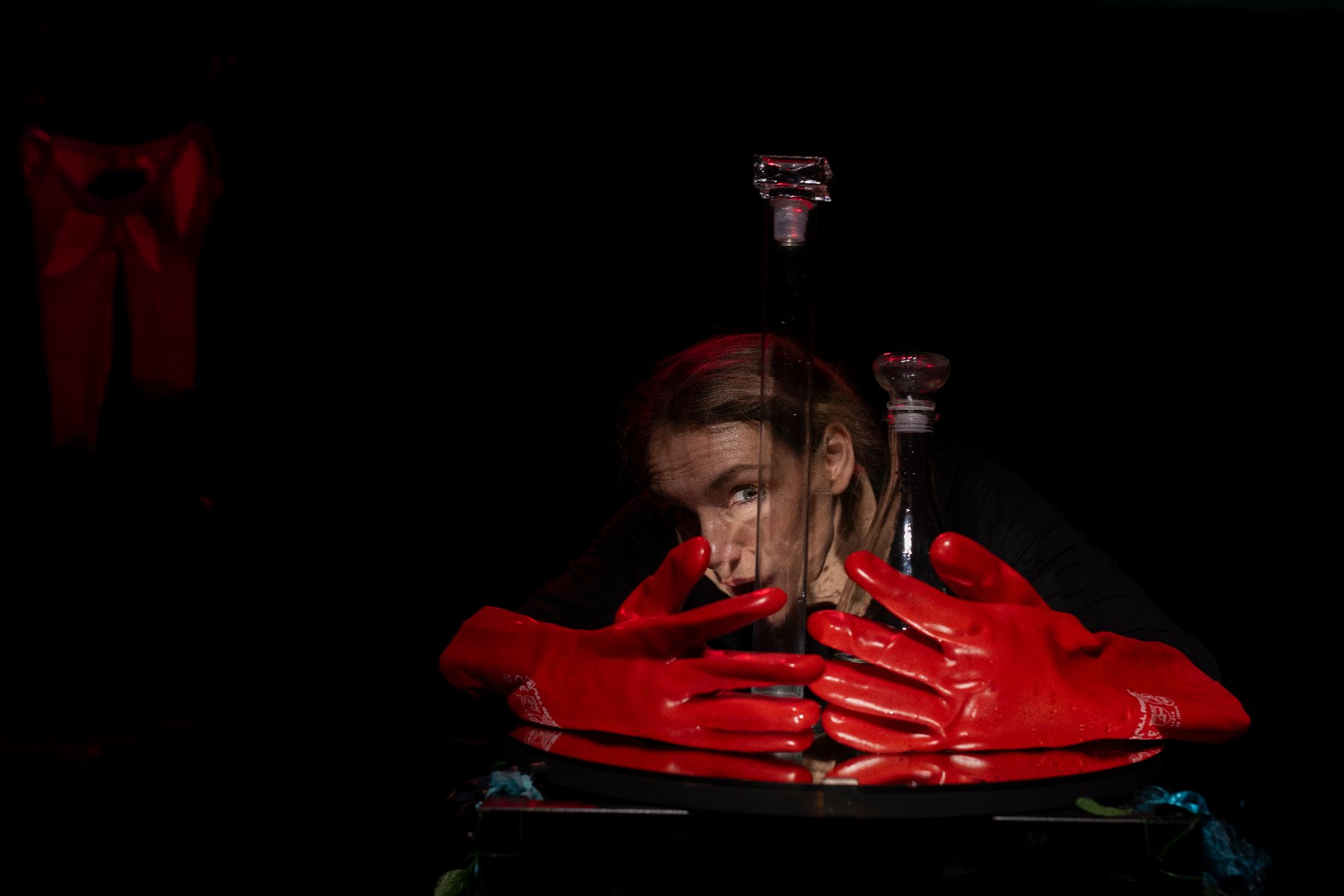 Na ciemnym tle twarz kobiety, przed nią duże czerwone rękawiczki.
