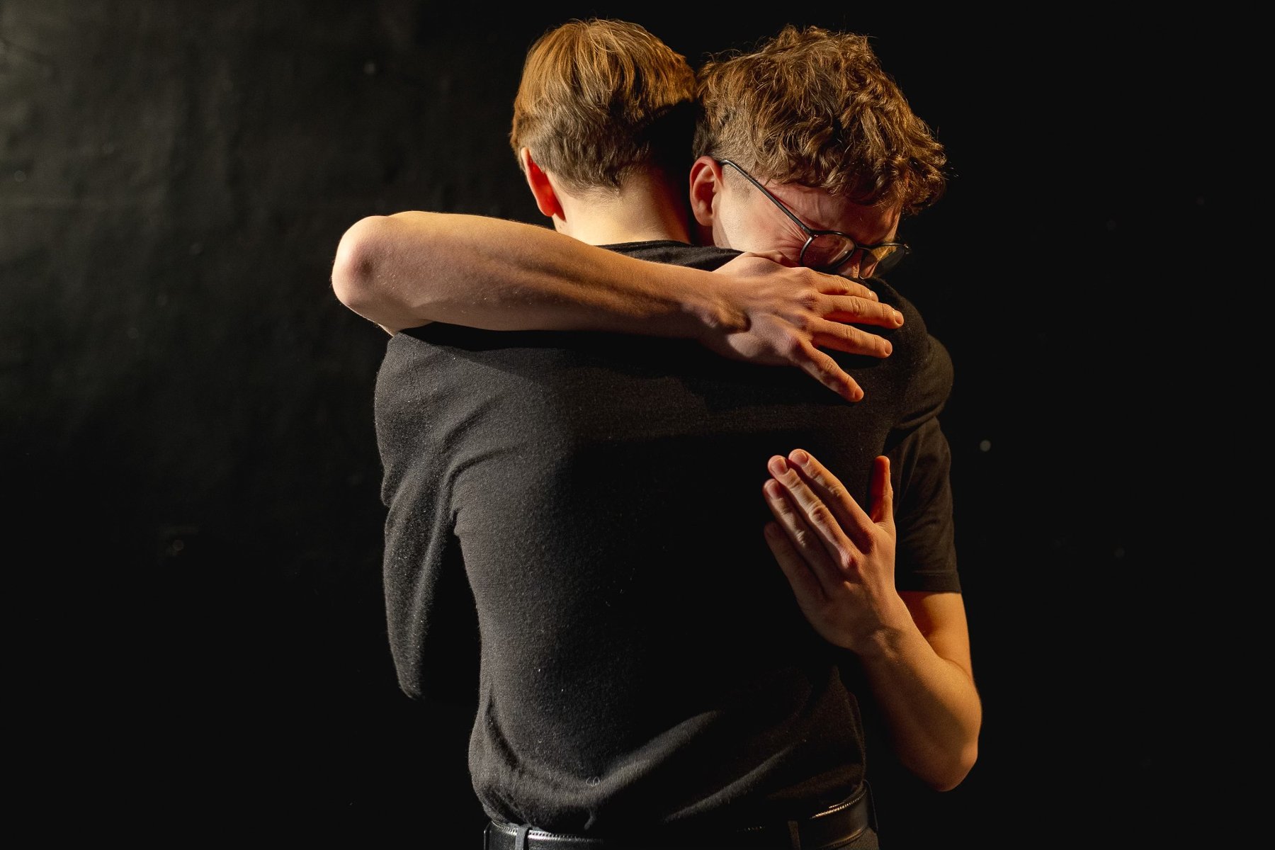 Dwóch mężczyzn przytulających się do siebie, ciemne tło.