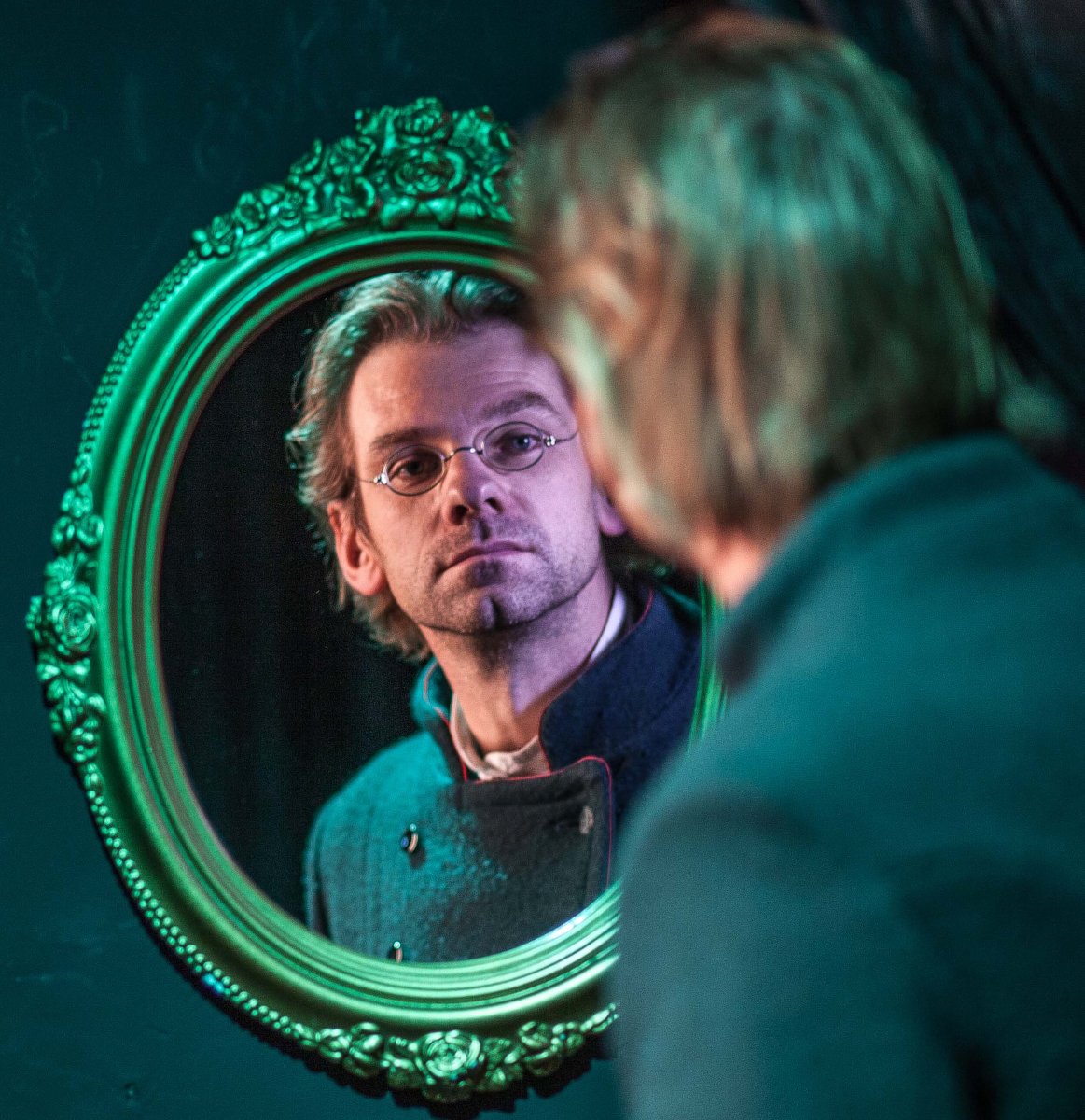 Zdjęcie mężczyzny przeglądającego się w lustrze ze zdobioną ramą.