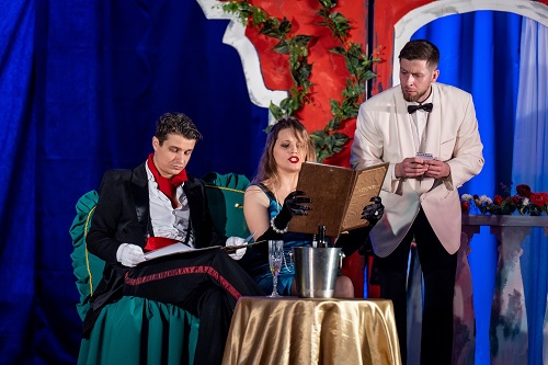 Przy stoliku siedzą kobieta i mężczyzna, oboje trzymają menu. Obok nich stoi kelner, który czeka na zamówienie.