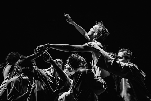 Czarno-białe zdjęcie mężczyzny z uniesionymi rękoma, który podtrzymywany jest przez kilka osób.