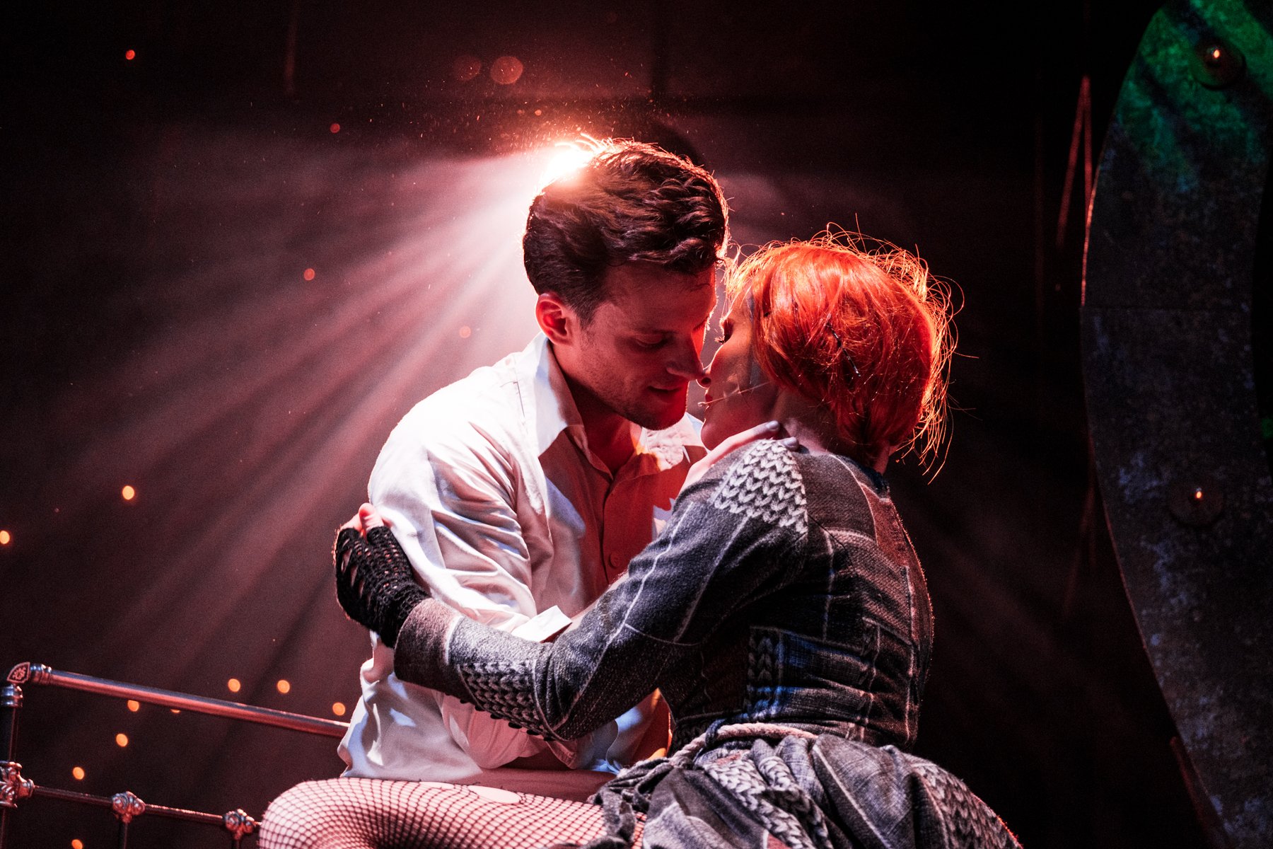 Zdjęcie obejmujących się kobiety i mężczyzny, ich twarze są blisko siebie. Z tyłu pada na nich rozproszone światło.