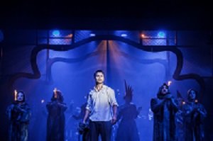 Zdjęcie w niebiesko-czarnych barwach: aktorzy na scenie, w centralnym pukcie mężczyzna w białej koszuli.