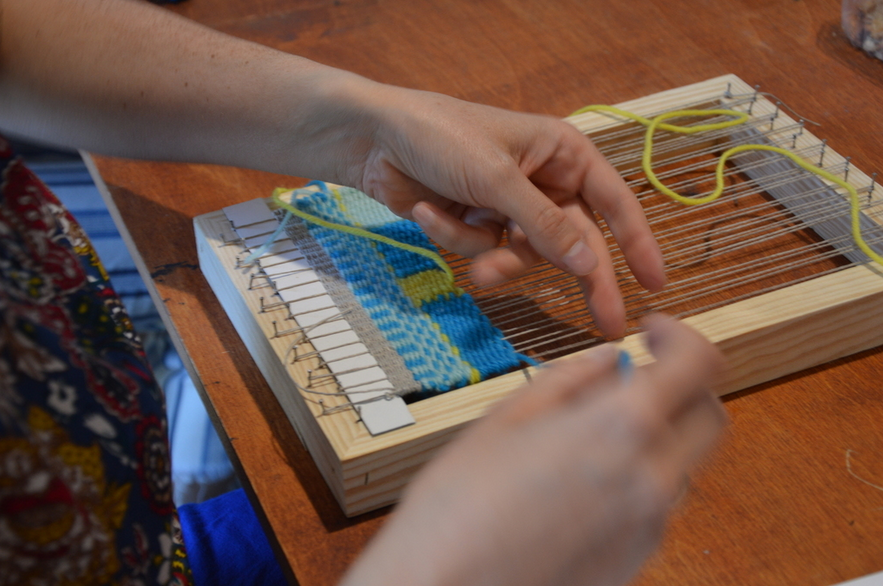 Dłonie wyplatające kolorową tkaninę na ręcznym, prostym krośnie.