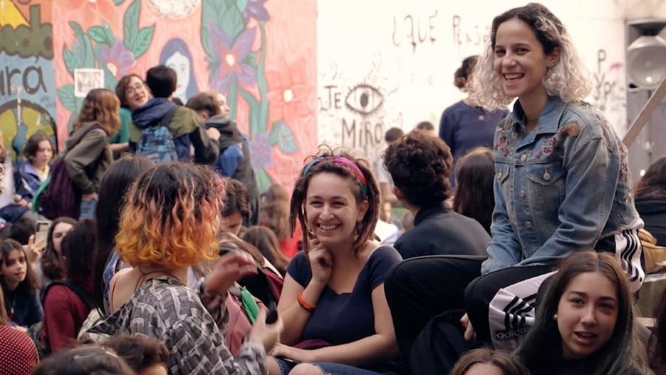 Grupa ludzi otoczonych ścianami z kolorowym grafitti. Z przodu grupa roześmianych dziewczyn.