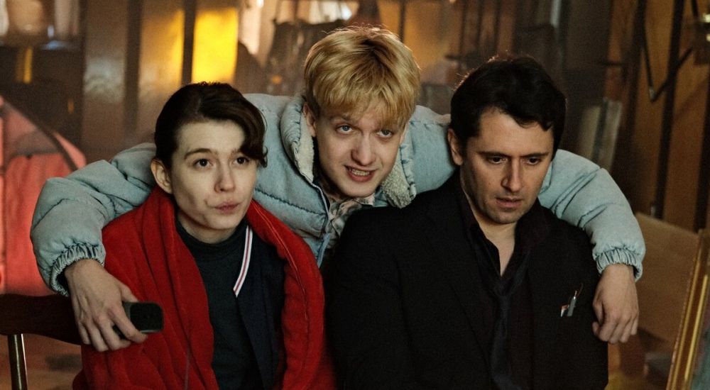 fot. materiały dystrybutora Mężczyzna pochyla się nad kobietą i mężczyzną, którzy siedzą na krzesłach. Obejmuje ich.