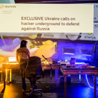 Dziewczyna stoi przed wielkim ekranem z napisem "Exclusive Ukraine calls on hacker undergroung to defend against Russia"