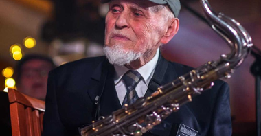 Zdjęcie Jana Ptaszyna Wróblewskiego w czapce z daszkiem, trzymającego saksofon.